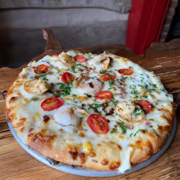A white pizza from The Humble Tomato, topped with shrimp, cherry tomatoes, and fresh herbs.