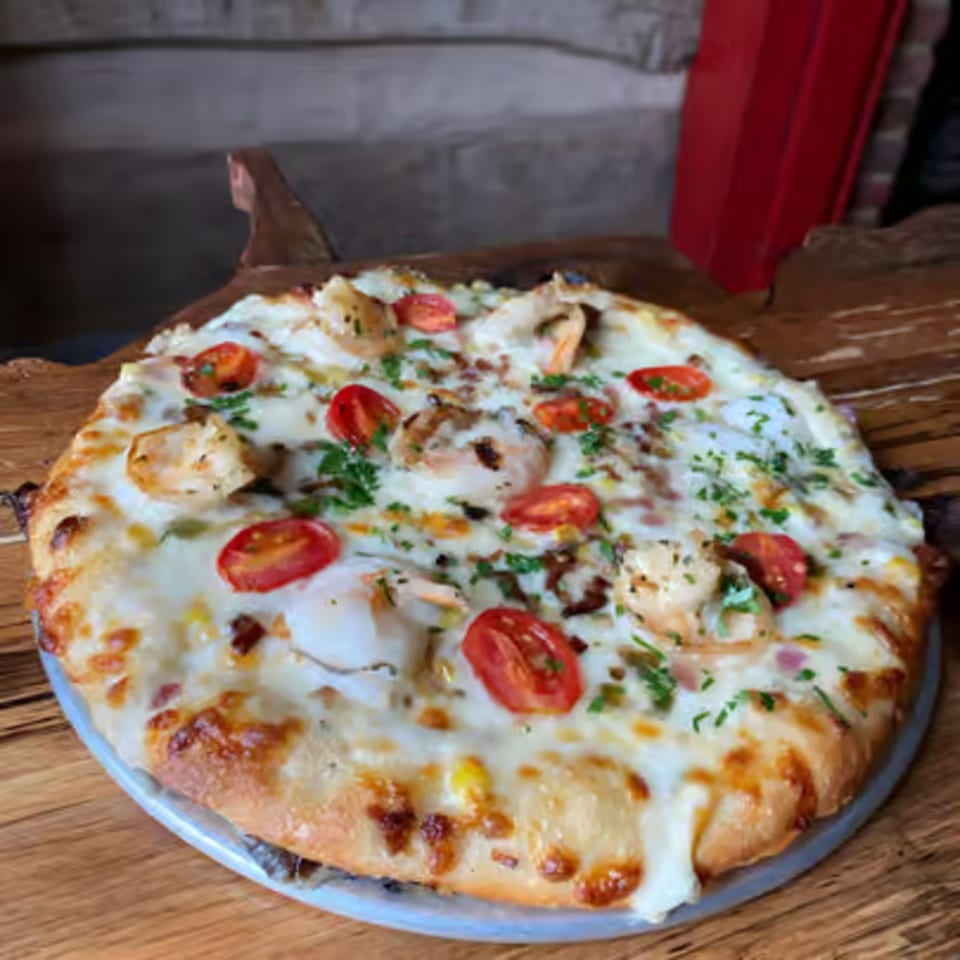 A white pizza from The Humble Tomato, topped with shrimp, cherry tomatoes, and fresh herbs.