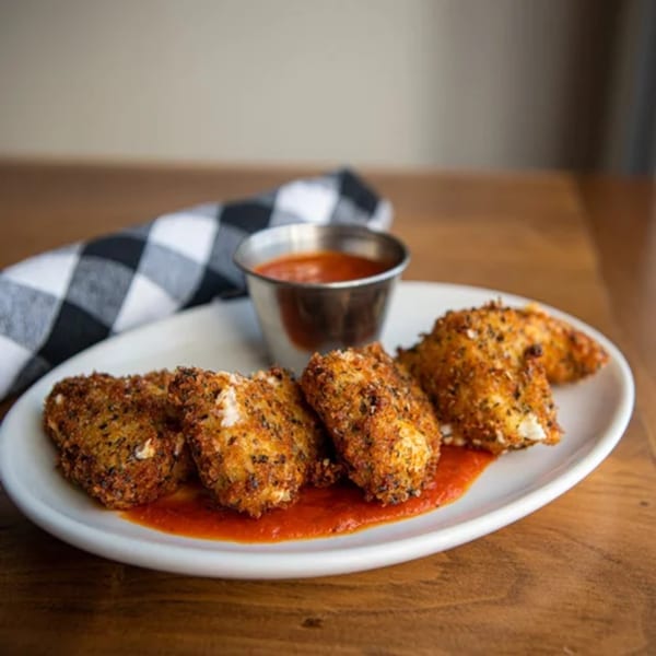 Crispy fried mozzarella sticks with marinara sauce on a white plate, next to a checkered napkin.