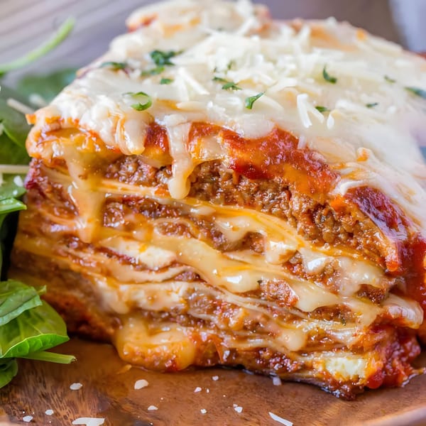 A close-up of a cheesy, layered lasagna with rich red sauce and ground meat, garnished with fresh greens.