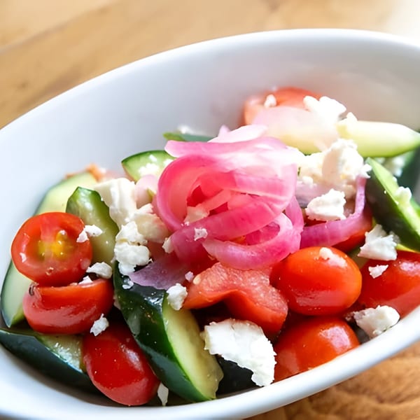 A fresh salad with cherry tomatoes, cucumber slices, pickled red onions, and crumbled feta cheese.