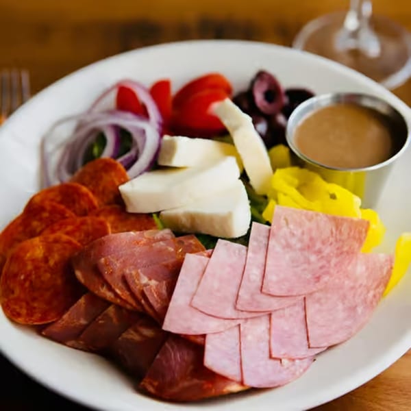 A Humble Tomato antipasto salad with pepperoni, salami, ham, mozzarella, onions, tomatoes, olives, and dressing.