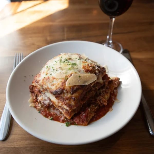 A plate of lasagna with melted cheese and red sauce, served with a glass of red wine.