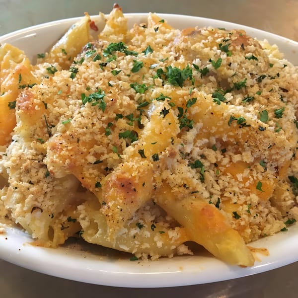 Baked penne pasta with melted cheese, breadcrumbs, and parsley in a white bowl.